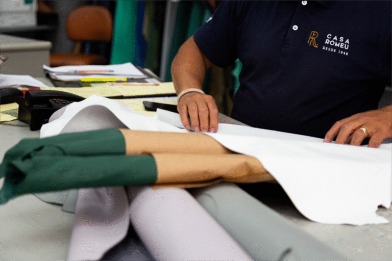 Profissional da Casa Romeu, vestindo camisa polo azul marinho com o logotipo da empresa e a inscrição "Desde 1948", manuseando e organizando peças de couro branco sobre uma mesa de trabalho.